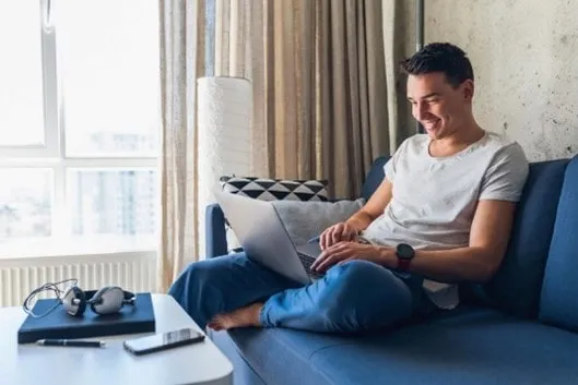 Spokojný mladý muž jednoducho kontaktuje službu preverenia vozidiel Vyberané autá online cez notebook z pohodlia domova.